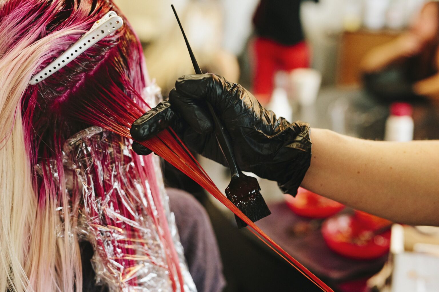 A hair colourist applying pink hair colour to a client's long blonde hair.